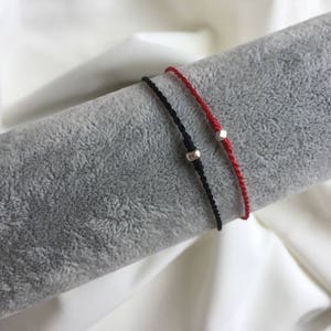 May include: Two friendship bracelets with silver beads. One bracelet is red and the other is black.