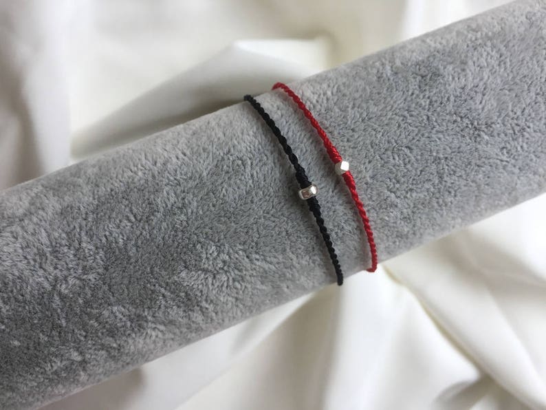 May include: Two friendship bracelets with silver beads. One bracelet is red and the other is black.