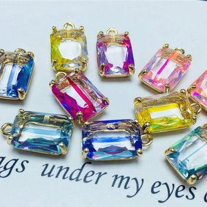 May include: Assortment of colorful, iridescent glass rectangular charms with gold-toned metal loops. The charms are perfect for jewelry making, crafting, and adding a touch of sparkle to any project.