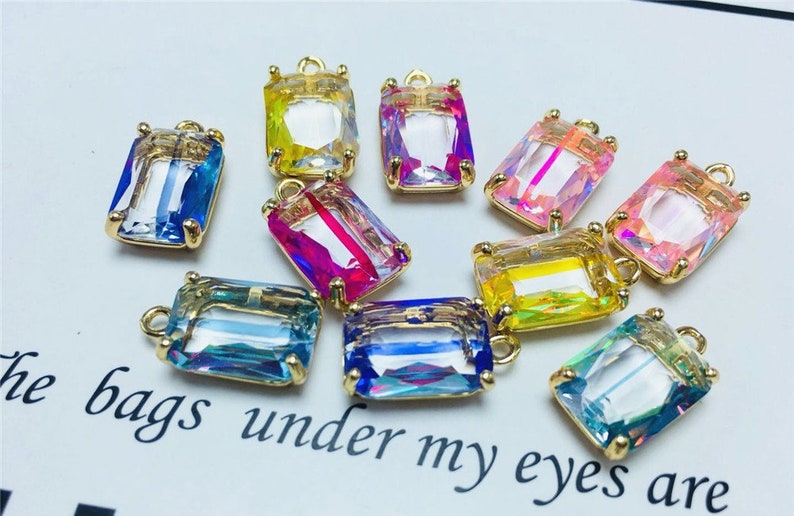 May include: Assortment of colorful, iridescent glass rectangular charms with gold-toned metal loops. The charms are perfect for jewelry making, crafting, and adding a touch of sparkle to any project.