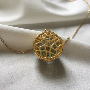 May include: A gold chain necklace with a round pendant featuring a delicate, intricate design. The pendant is filled with a light blue and green material.