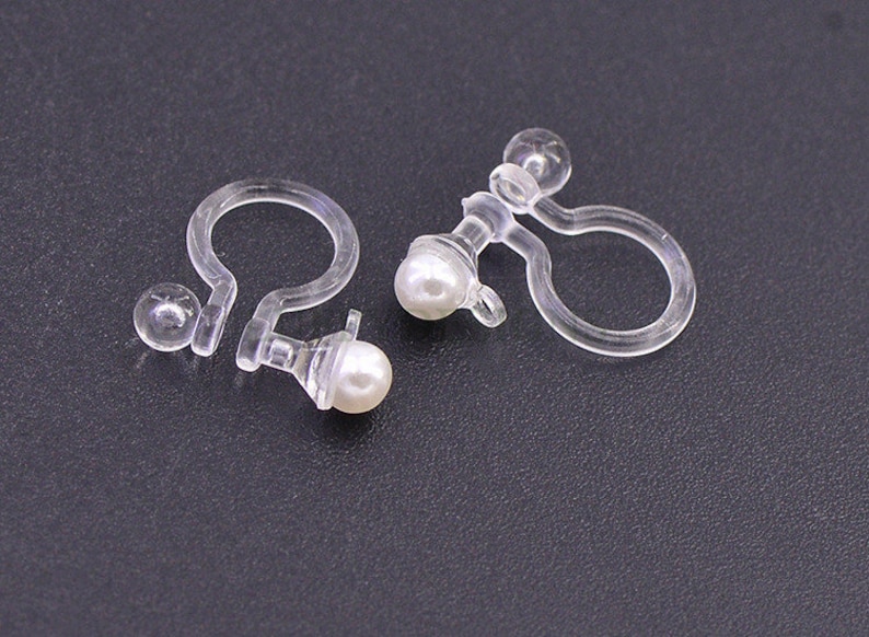 May include: A pair of clear plastic earring clips with a pearl-like bead on each clip.