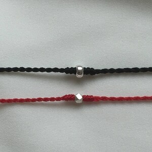 May include: Two braided cords with silver bead accents. The top cord is black and the bottom cord is red.