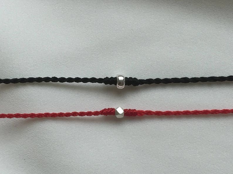 May include: Two braided cords with silver bead accents. The top cord is black and the bottom cord is red.