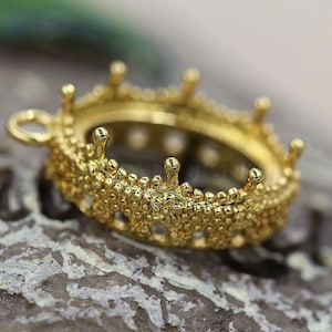 Peut inclure: Pendentif en métal doré en forme de couronne avec une ouverture ronde pour une pierre ou un camée. Le pendentif a une surface texturée et une boucle pour attacher une chaîne.