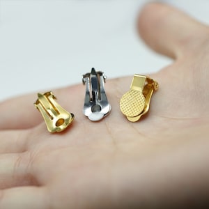 Op de afbeelding: Drie oorclips, één gouden, één zilveren en één met een gouden afwerking. De clips zijn ontworpen om oorbellen op hun plaats te houden.