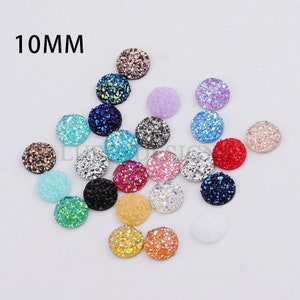 May include: Assortment of 10mm round, flat-backed, glitter cabochons in various colors, including blue, green, pink, purple, red, and silver.