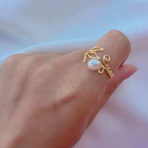 May include: A gold wire ring featuring a single white pearl. The ring is delicate and has a unique design.