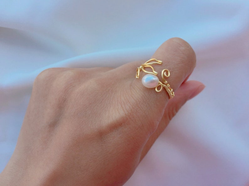 May include: A gold wire ring featuring a single white pearl. The ring is delicate and has a unique design.