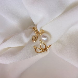 May include: A gold wire ring with a delicate floral design and a white pearl accent.
