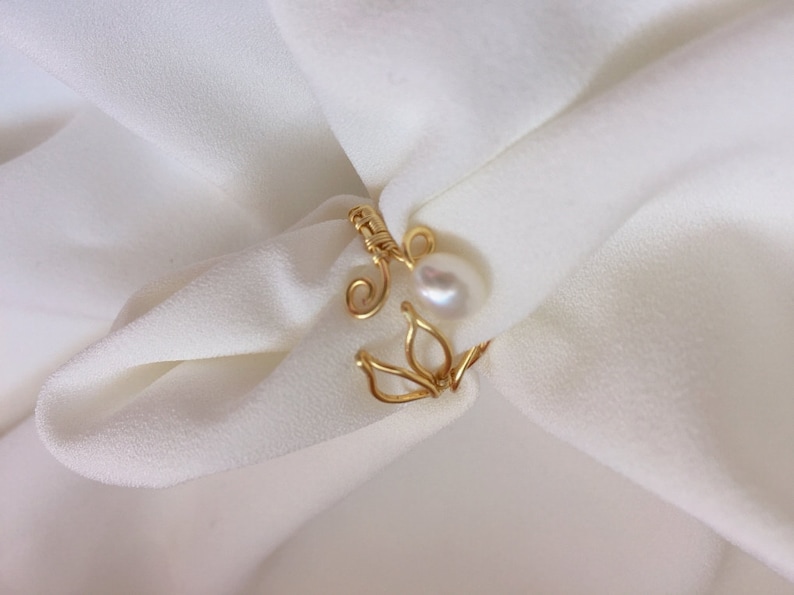 May include: A gold wire ring with a delicate floral design and a white pearl accent.
