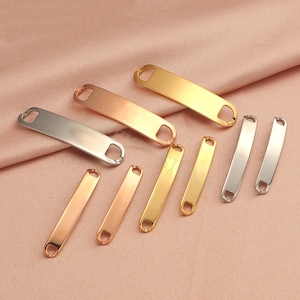 May include: A set of eight metal tag blanks in silver, gold, and rose gold. The tags are rectangular with rounded edges and have two holes at each end.