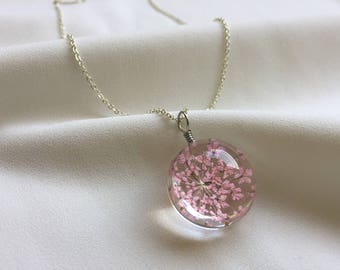May include: A silver chain necklace with a round pendant featuring a delicate pink flower pressed inside clear resin.