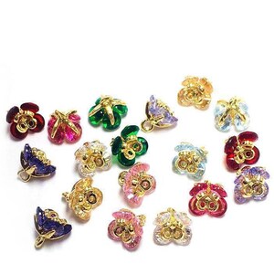 May include: Assortment of colorful flower-shaped metal charms with crystal accents. The charms are gold-toned and feature various colors, including red, green, blue, pink, and purple.
