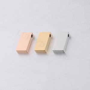 Puede incluir: Tres abalorios rectangulares de metal en oro rosa, oro y plata. Cada abalorio tiene un pequeño agujero en la parte superior para sujetarlo a un collar o pulsera.