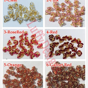 May include: Assortment of 20 gold-tone metal flower-shaped charms with crystal accents in six colors: clear, pink, rose red, red, orange, and garnet red.