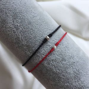 May include: Two friendship bracelets with silver beads. One bracelet is red and the other is black.
