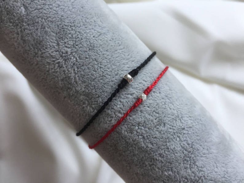 May include: Two friendship bracelets with silver beads. One bracelet is red and the other is black.
