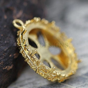 May include: Gold-toned metal pendant setting with a decorative, ornate design. The setting is designed to hold a round cabochon stone.