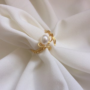 May include: A gold wire ring featuring a single white pearl. The ring is delicate and has a simple design.