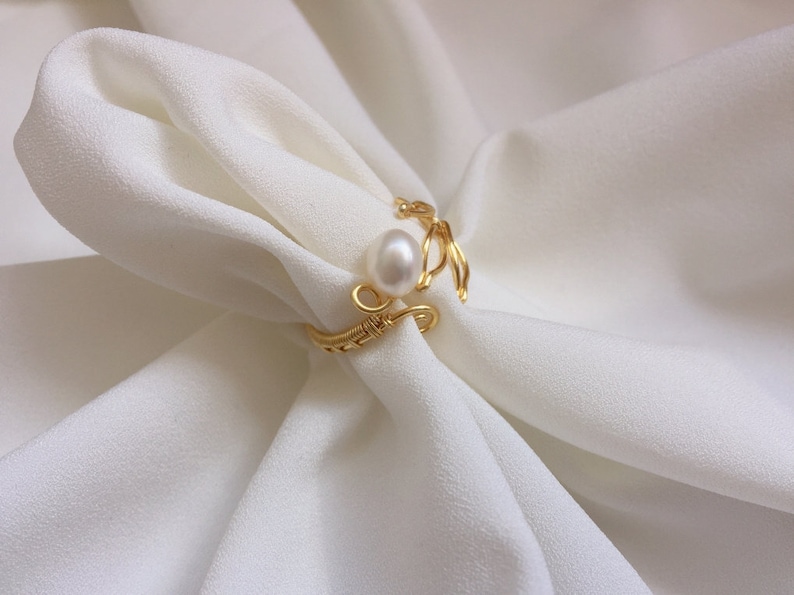 May include: A gold wire ring featuring a single white pearl. The ring is delicate and has a simple design.