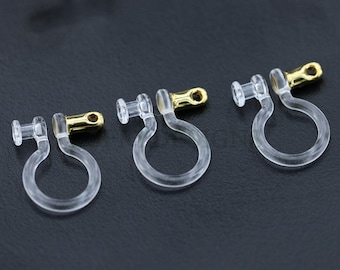 May include: Three clear plastic earring backs with gold-colored metal clips. The backs are designed to hold earrings in place.