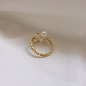May include: A gold wire ring with a pearl accent. The ring is made of thin wire that is twisted and woven together to create a delicate and intricate design. The pearl is a small, white pearl that is set in the centre of the ring.