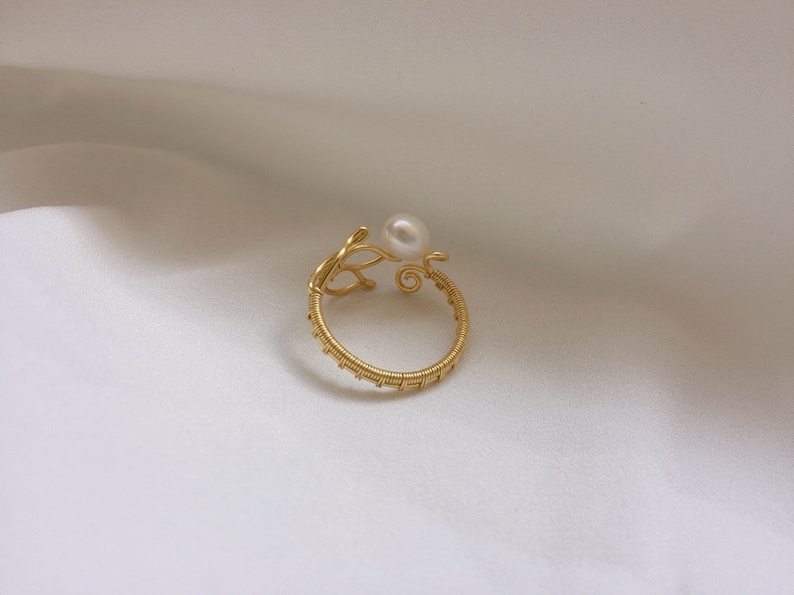 May include: A gold wire ring with a pearl accent. The ring is made of thin wire that is twisted and woven together to create a delicate and intricate design. The pearl is a small, white pearl that is set in the centre of the ring.