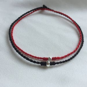 May include: A red and black string bracelet with a silver bead charm.