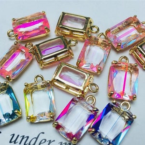 May include: Assortment of 12 gold-toned rectangular pendant charms with iridescent glass inserts. The charms have a variety of colors including pink, blue, and clear.