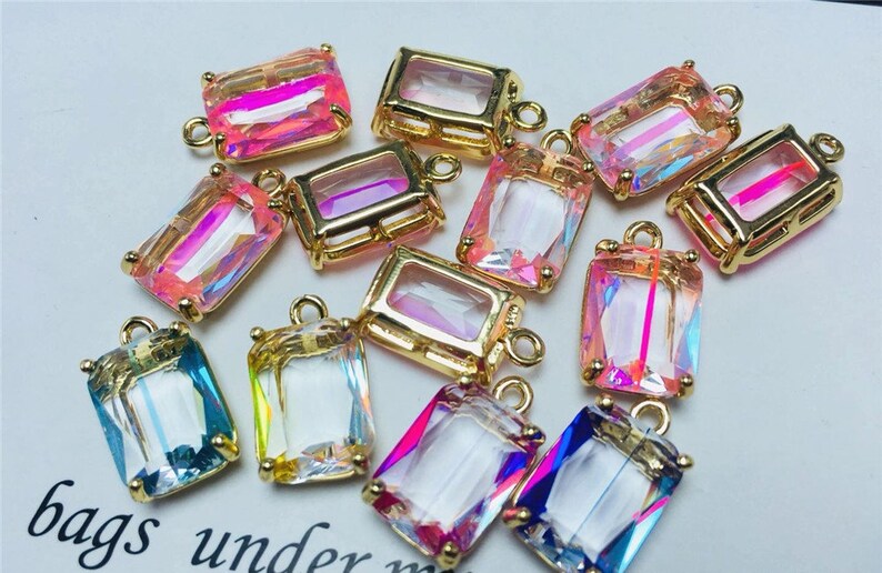 May include: Assortment of 12 gold-toned rectangular pendant charms with iridescent glass inserts. The charms have a variety of colors including pink, blue, and clear.