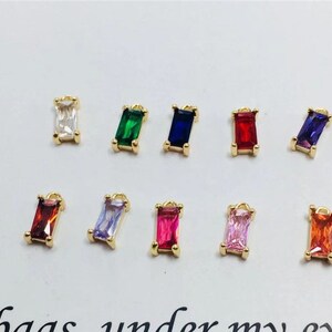 May include: Ten gold charms with different colored rectangular gemstones. The charms are perfect for jewelry making and crafting.