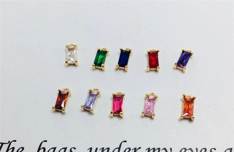 May include: Ten gold charms with different colored rectangular gemstones. The charms are perfect for jewelry making and crafting.