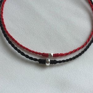 May include: A red and black string bracelet with a silver bead charm.