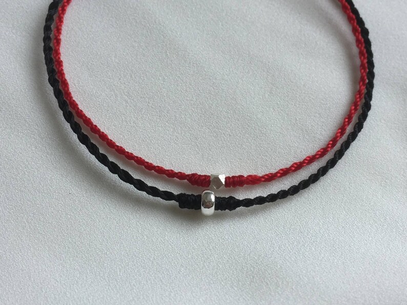 May include: A red and black string bracelet with a silver bead charm.