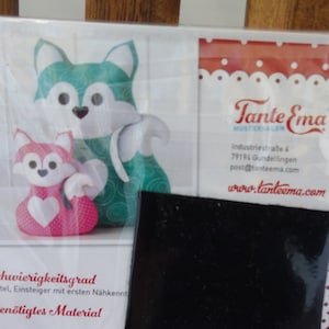 Könnte beinhalten: Ein Schnittmuster-Paket mit Anleitungen für zwei Fuchs-Plüschtiere. Ein Fuchs ist türkis-weiß, der andere rosa mit Herz. Das Paket enthält den Text "Tante Ema" und Maße in cm: 25 x 45 cm und 40 x 73 cm.