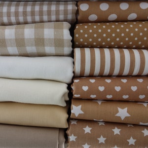 Könnte beinhalten: Ein Stapel Stoffmuster in verschiedenen Beige- und Brauntönen. Die Stoffe haben verschiedene Muster, darunter Gingham, Punkte, Streifen, Herzen und Sterne.