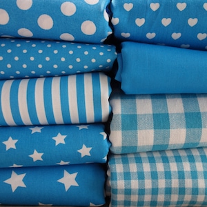 Könnte beinhalten: Ein Stapel blauer Stoffrollen mit verschiedenen weißen Mustern, darunter Punkte, Herzen, Streifen, Sterne und Vichy-Karo. Die Stoffe sind ordentlich gefaltet und zeigen eine Reihe von Texturen und Designs, die sich für Nähprojekte eignen.