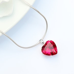 May include: A silver chain necklace with a large, red heart-shaped pendant.