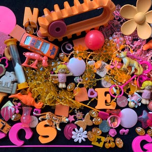 May include: A vibrant collection of orange and pink decorative items, including letters, beads, toys, and floral accents. The assortment features a toy car, a small hourglass, and the text "the warhol".