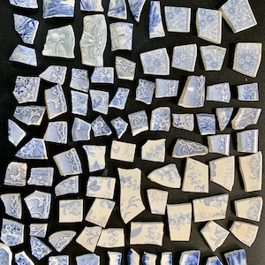 May include: A collection of numerous ceramic shards featuring blue and white patterns. The fragments display various intricate floral, geometric, and scrollwork designs on white backgrounds, with irregular shapes and jagged edges throughout.