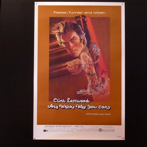 May include: A movie poster for the film "Any Which Way You Can" starring Clint Eastwood. The poster features a close-up of Clint Eastwood's face, with the title of the film in large, bold letters below. The poster is set against a yellow background.