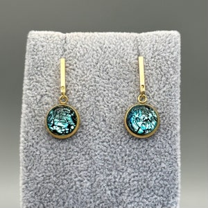 May include: A pair of gold dangle earrings with a round blue and black iridescent glass stone on each earring.