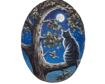 Hand painted pebble Cat sitting on a tree branch under the moon in a night sky background! Cat mini painting on a flat natural sea pebble.
