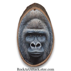 May include: A close-up painting of a gorilla's face on a wooden slice. The gorilla has dark brown eyes and a serious expression. The painting is signed "L. Kanetis" in the bottom right corner.
