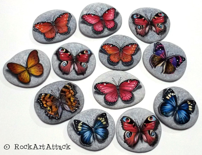 May include: Hand-painted butterfly art on smooth, gray stones. Each stone features a unique butterfly design in vibrant colors like red, orange, blue, and purple. The artwork is detailed and realistic, showcasing the beauty of nature.