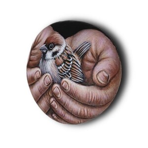 May include: A circular painting featuring a detailed brown and white sparrow nestled within two cupped hands. The bird has distinct black markings on its face and wings, while the hands are rendered in realistic skin tones against a dark background.