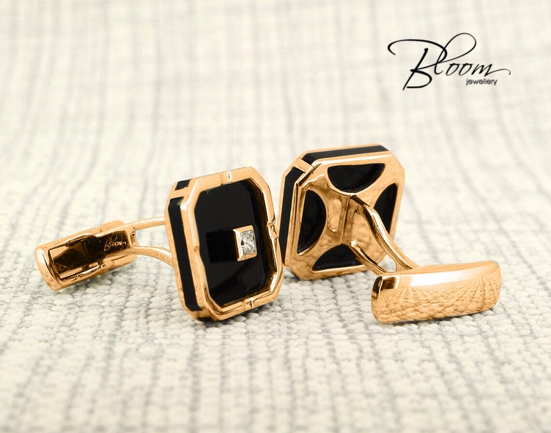 May include: A pair of gold-toned cufflinks with black square insets and a small diamond accent. The cufflinks have a rectangular shape with rounded corners and a polished finish. The Bloom jewellery logo is visible in the image.