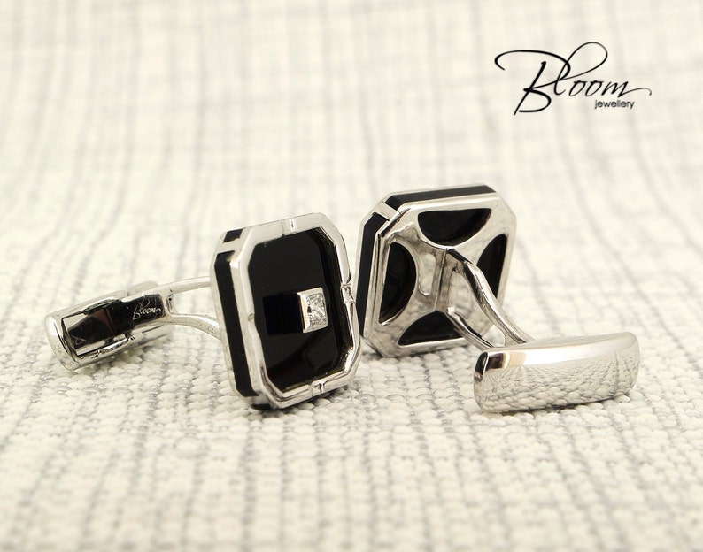 May include: A pair of silver cufflinks with black rectangular insets and a small square diamond. The cufflinks have a polished finish and are set against a textured, off-white background. The Bloom Jewellery logo is visible.