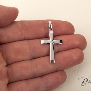 K&ouml;nnte beinhalten: Ein silberner Kreuzanh&auml;nger mit einem schlichten, geometrischen Design. Das Kreuz wird in einer Hand gehalten, wodurch seine Gr&ouml;&szlig;e und Details hervorgehoben werden.